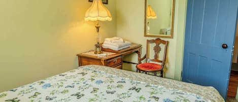 Un dormitorio con cama, mesita de noche, silla, lámpara y puerta.