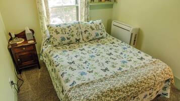 Un dormitorio con cama, mesita de noche, lámpara, radiador y ventana con cortinas.