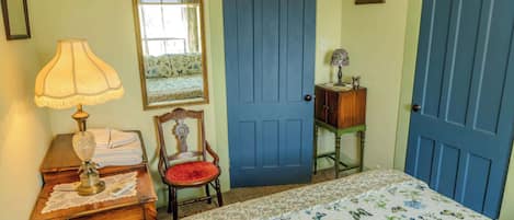 A bedroom with a bed, a chair, a dresser, a lamp, a mirror, and a door.