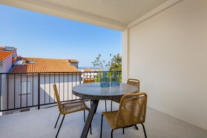 Taula rodona amb quatre cadires de vimetta a un balcó amb vista despejada a edificis i arbres.