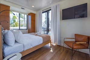 Un dormitorio moderno con una cama de madera, un televisor montado en la pared y vistas al exterior a través de un amplio ventanal.