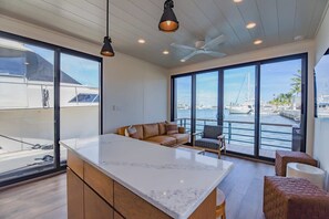Una cocina moderna con una isla grande, un área de estar con sofá y sillas, y ventanas amplias con vista al puerto deportivo.