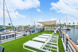 Un puerto deportivo con barcos, una terraza cubierta de césped con sillones de descanso y un cielo despejado.