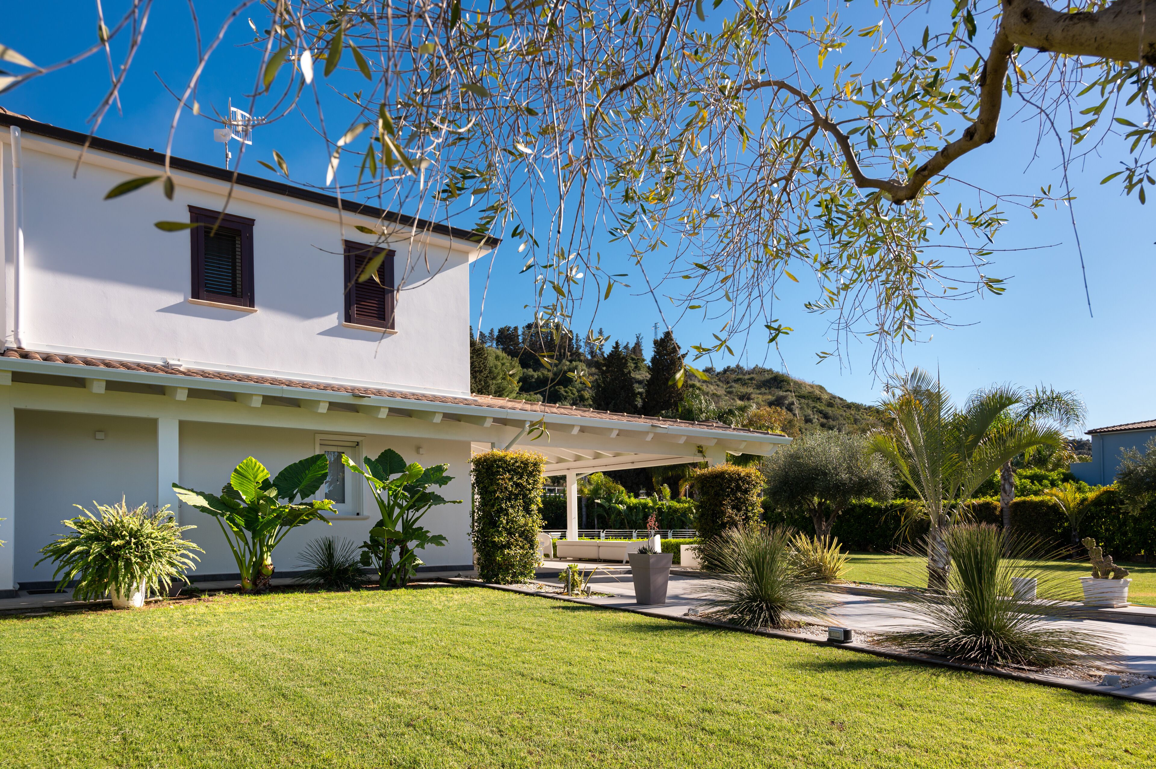 A white building with a covered patio, surrounded by well-maintained greenery and a clear blue sky.