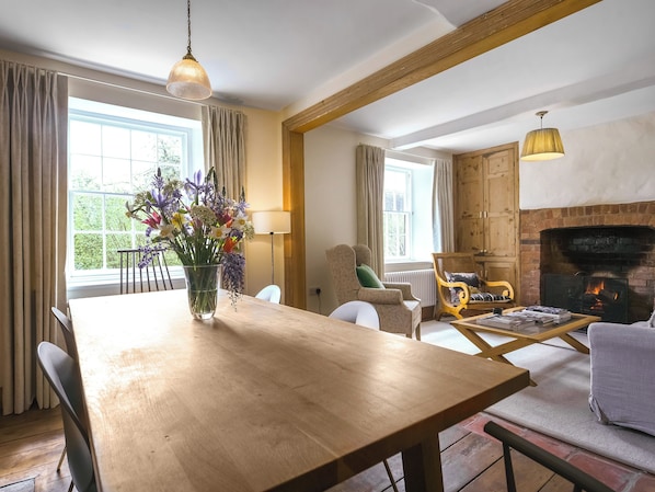 Ein geräumiges Wohnzimmer mit Esstisch aus Holz, bequemen Sitzgelegenheiten, einem Kamin und großen Fenstern.