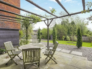 Eine Terrassengruppe im Freien mit einem Holztisch und vier Stühlen, umgeben von einer Ziegelwand und einer Holzpergola.