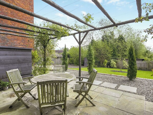 An outdoor patio with a wooden table and four chairs, surrounded by a brick wall and a wooden pergola. - 2 bedroom accommodation in Ludlow (Ludlow)