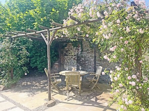 Un patio jardín con pérgola, pared de piedra y mobiliario exterior.