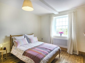 Ein Schlafzimmer mit einem hölzernen Bett, weißen Wänden, einem Fenster mit Vorhängen und einer Heizung.