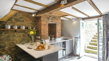 A kitchen with exposed wooden beams, stone walls, and a view of a stone staircase outside.