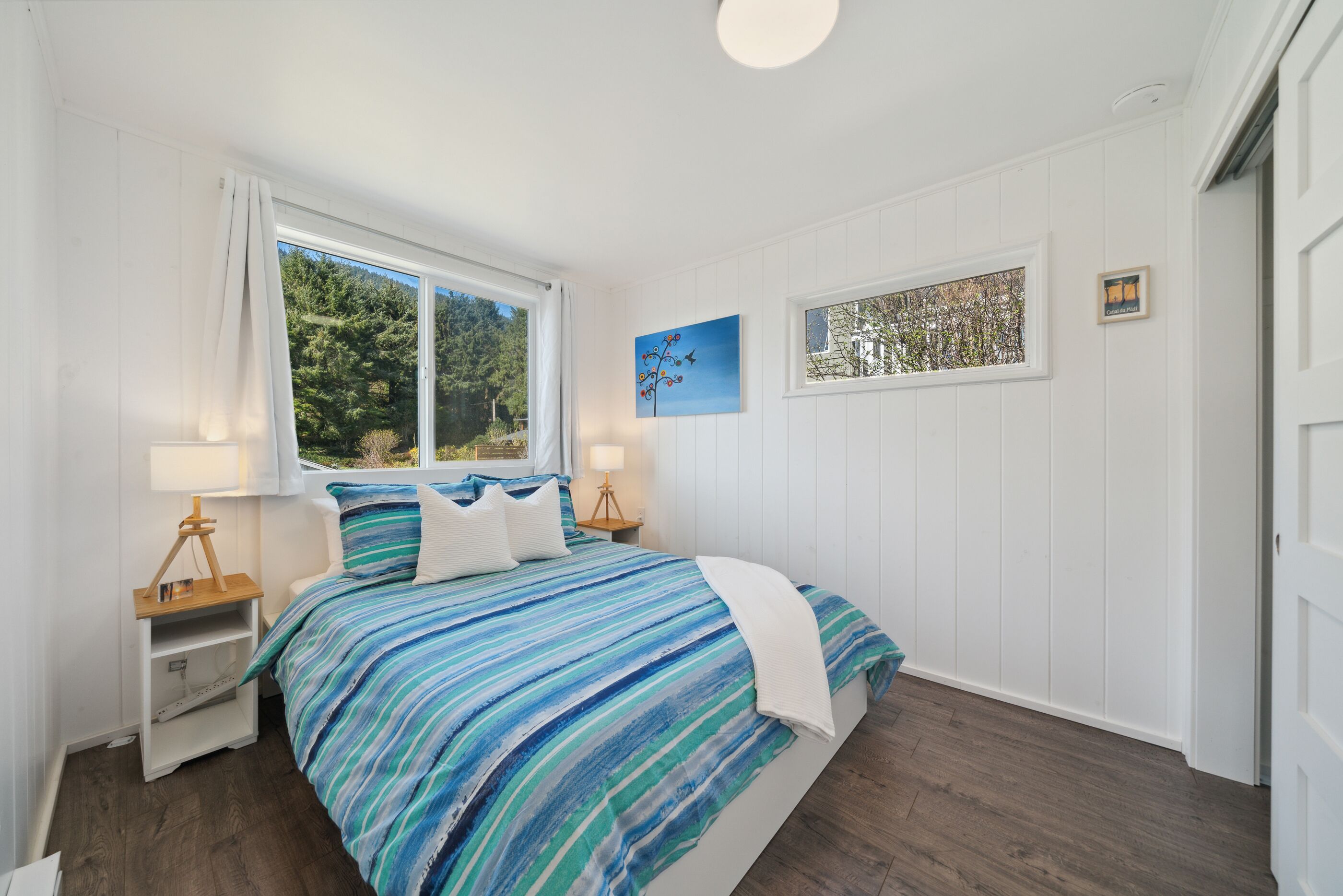 A bedroom with a bed, a nightstand, a window, and a painting on the wall.