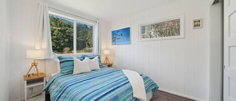 A bedroom with a bed, a nightstand, a window, and a painting on the wall.