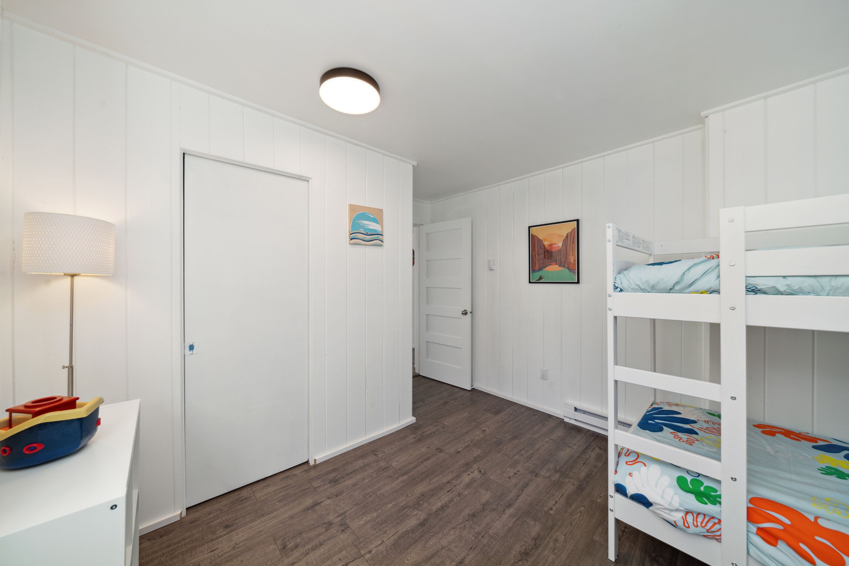 Une chambre d’enfant avec des lits superposés, un bureau sur lequel est posé un bateau jouet et une lampe.