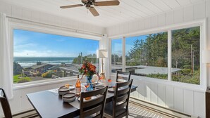 A dining area with a table set for four, large windows offering a view of the ocean and nearby buildings. - Treasure Hideaway-Manzanita Or., Ocean View,Fenced Yard, Arcade games, Dog Ok (Nehalem)