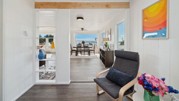 A modern interior with a dining area, a seating area with a chair and a vase of flowers, and a view through an open door to a balcony. - Treasure Hideaway-Manzanita Or., Ocean View,Fenced Yard, Arcade games, Dog Ok (Nehalem)