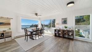 A spacious room with a large dining table, dark wooden chairs, a white ceiling fan, and a view of the ocean. - Treasure Hideaway-Manzanita Or., Ocean View,Fenced Yard, Arcade games, Dog Ok (Nehalem)
