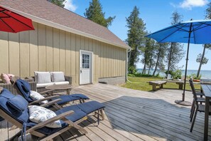 A wooden deck with lounge chairs and a table, a door, and a view of the water. - Waterfront Lake Michigan Tranquility Bay Getaway (Sister Bay)