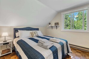 A bedroom with a bed, bedside table, lamp, and a window with a view of trees. - Waterfront Lake Michigan Tranquility Bay Getaway (Sister Bay)