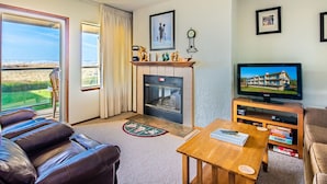 A living room with a fireplace, a television, a leather sofa, and a view of the outdoors.