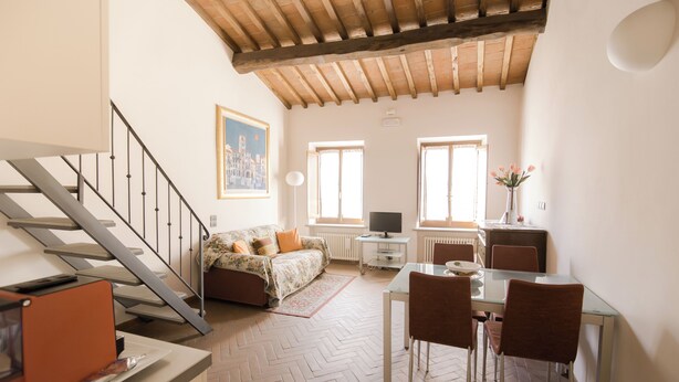 A spacious living area with a herringbone-patterned floor, a wooden ceiling, a sofa, a dining table with chairs, and a staircase.