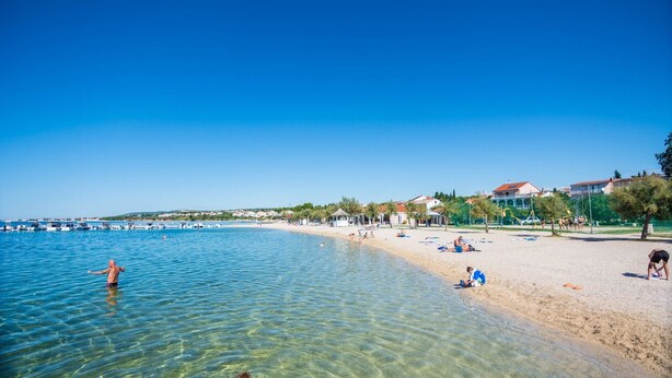 Une plage avec une eau claire et peu profonde, un rivage sablonneux et quelques personnes qui se détendent.