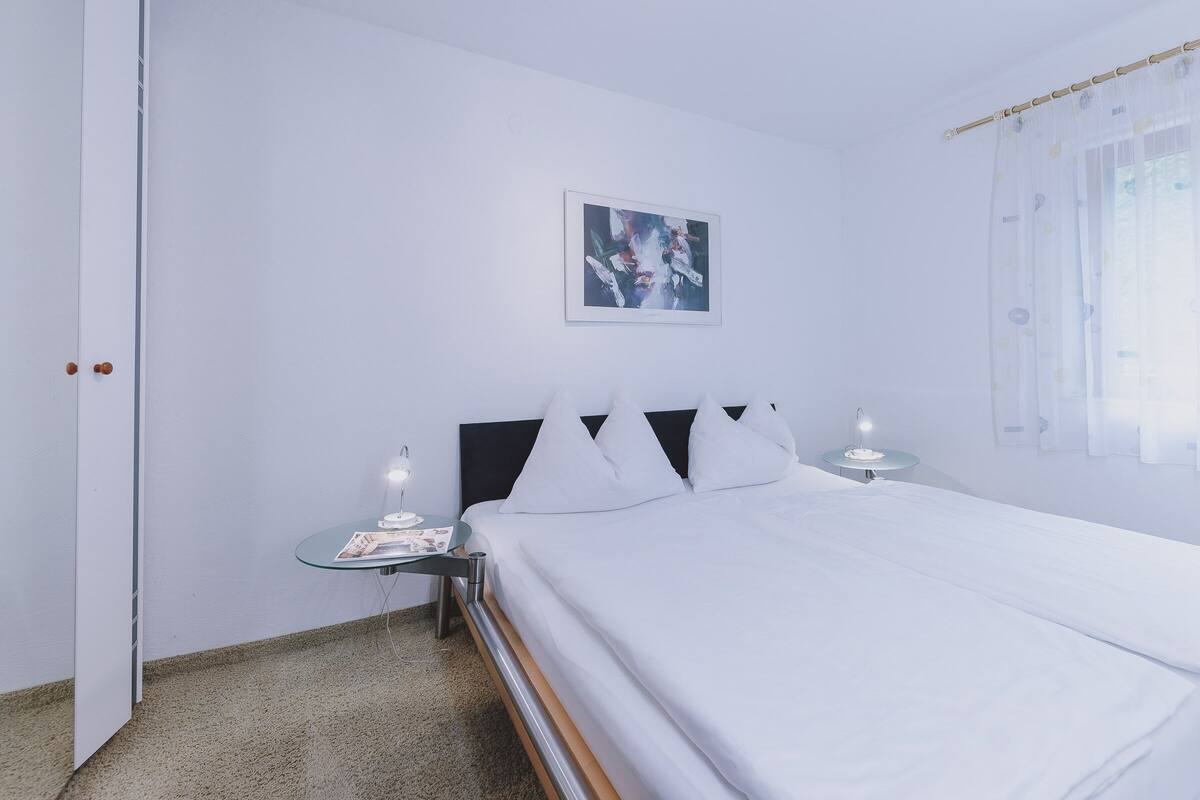 Ein Hotelzimmer mit einem Bett, zwei Nachttischen, einer Tür und einem Fenster mit transparenten Vorhängen.