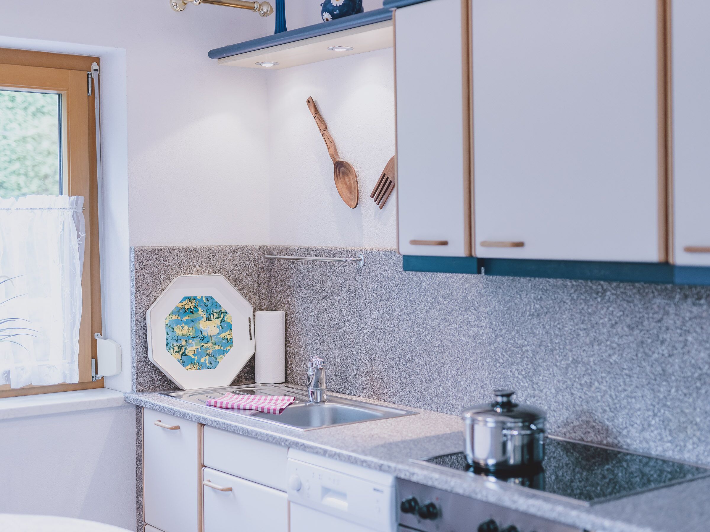 Une cuisine avec des armoires blanches, un plan de travail en granit, un évier, une cuisinière et des ustensiles de cuisine en bois accrochés au mur.