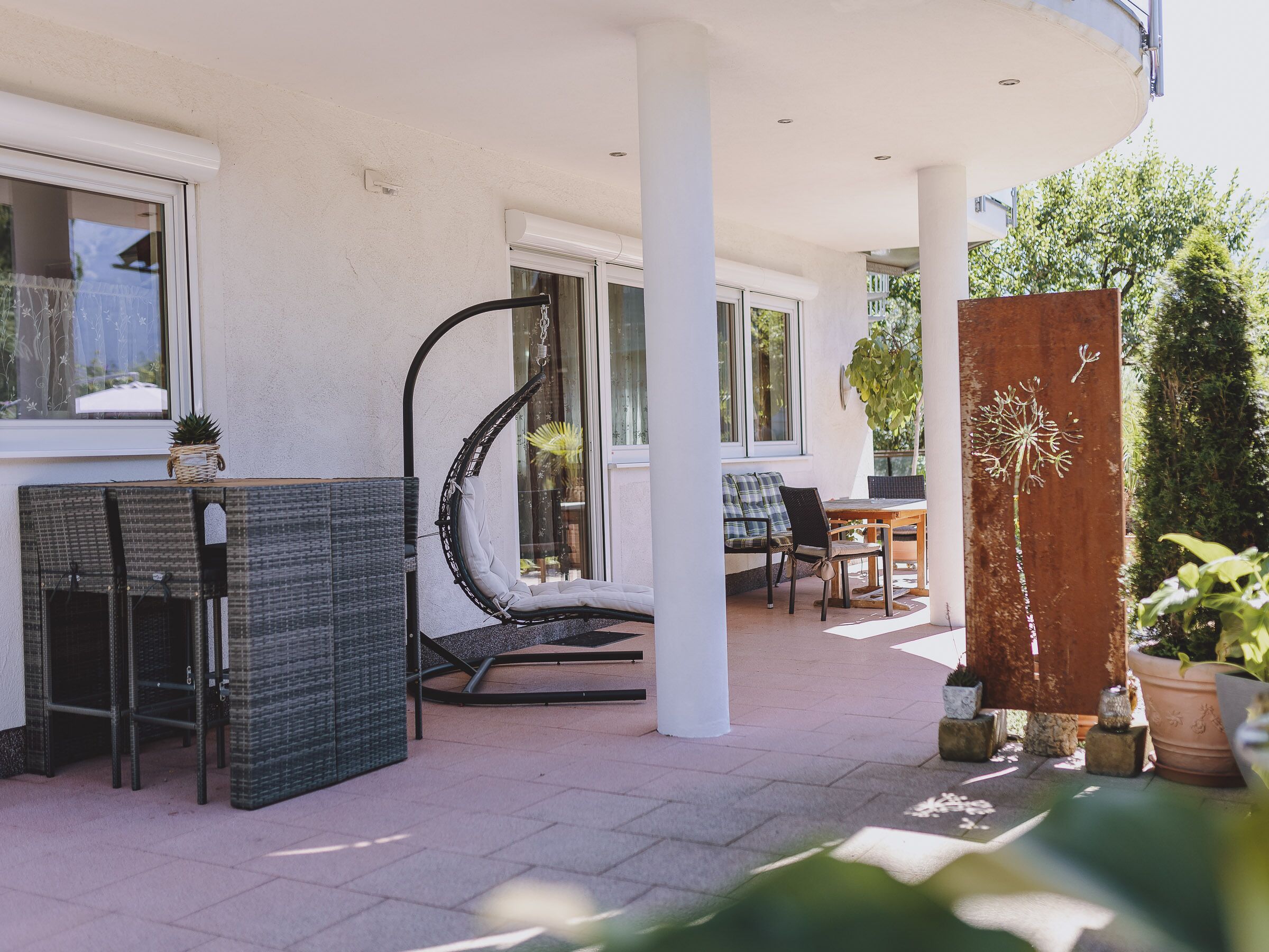 Zona patio esterna con tavolo, sedie, una sedia a dondolo e piante in vaso.