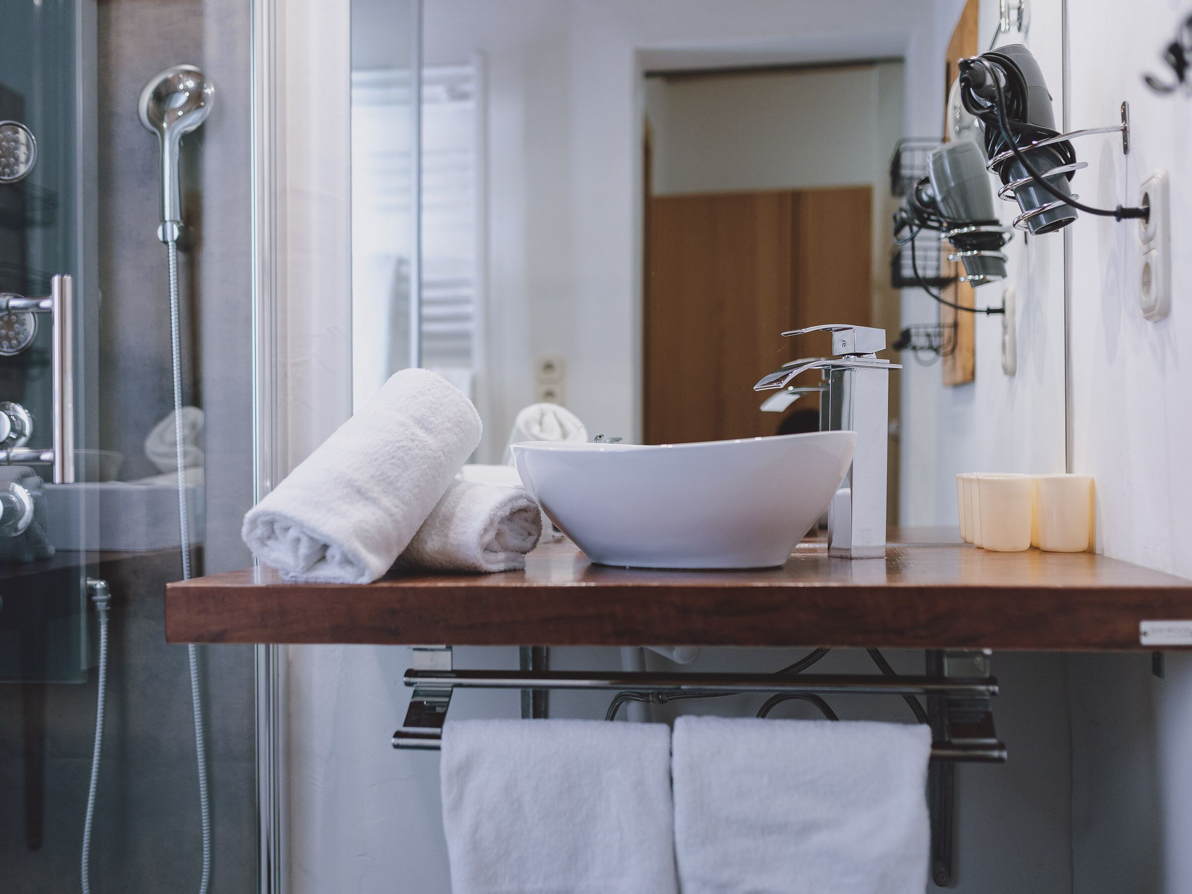 A bathroom with a glass shower enclosure, a white sink, and a towel rack.