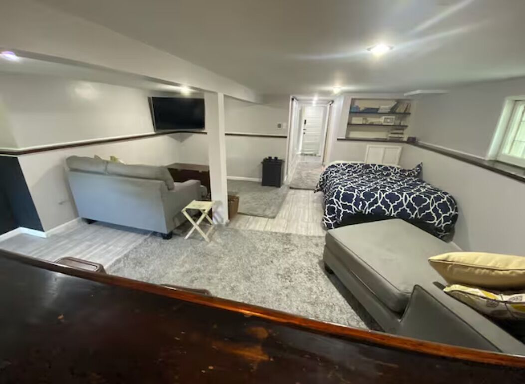 Een kleine slaapkamer met een bed, een slaapbank, een tafeltje en een televisie die aan de muur is bevestigd.