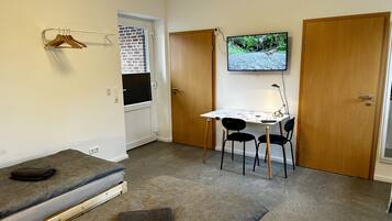 Een kleine kamer met een bed, een bureau met twee stoelen, een televisie aan de muur en een deur.