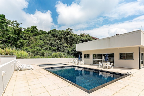 A swimming pool with lounge chairs and a table, surrounded by a building with large windows.