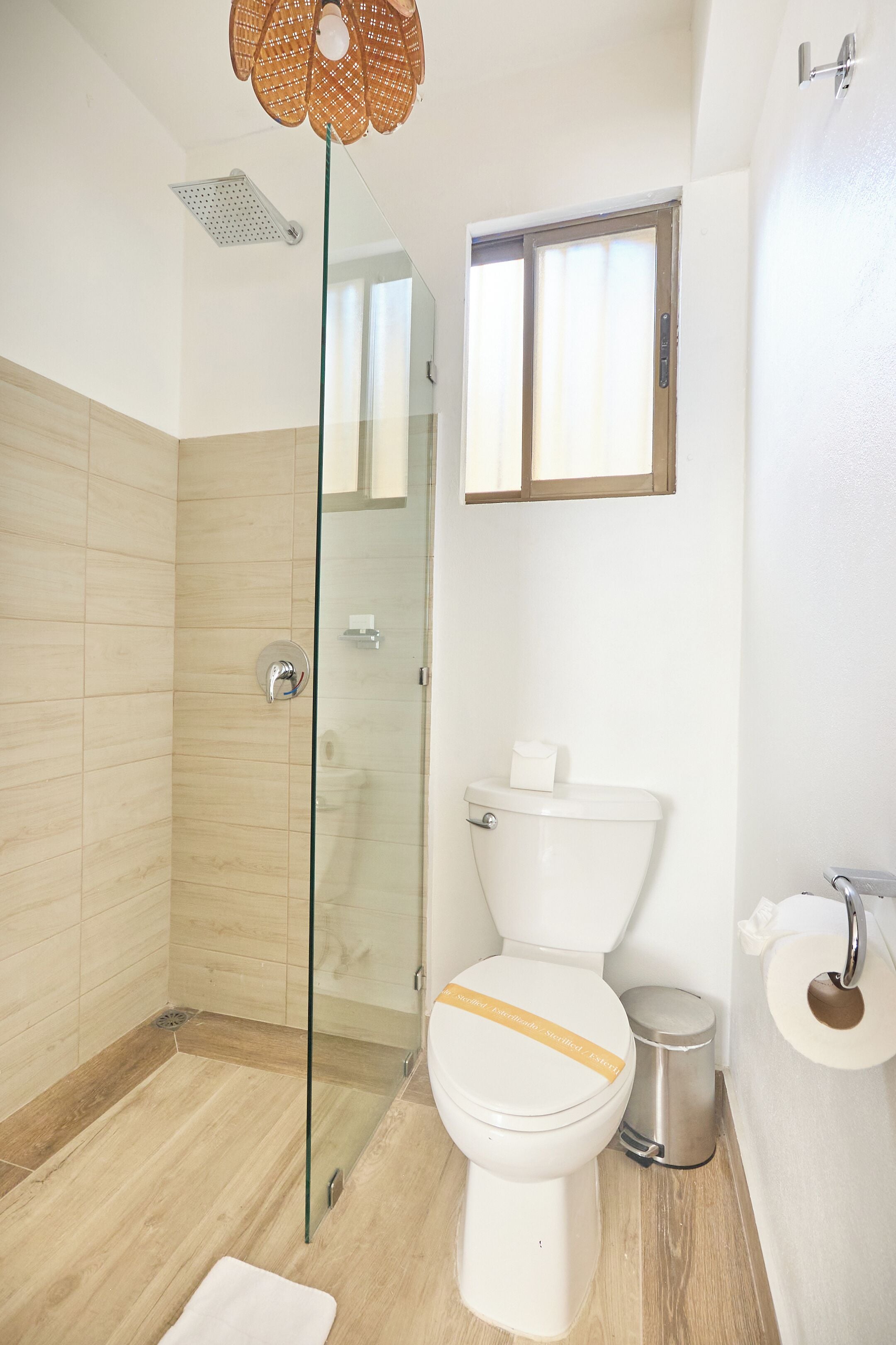 A modern bathroom with a glass shower enclosure, a toilet with a yellow stripe, and a small window above the toilet.