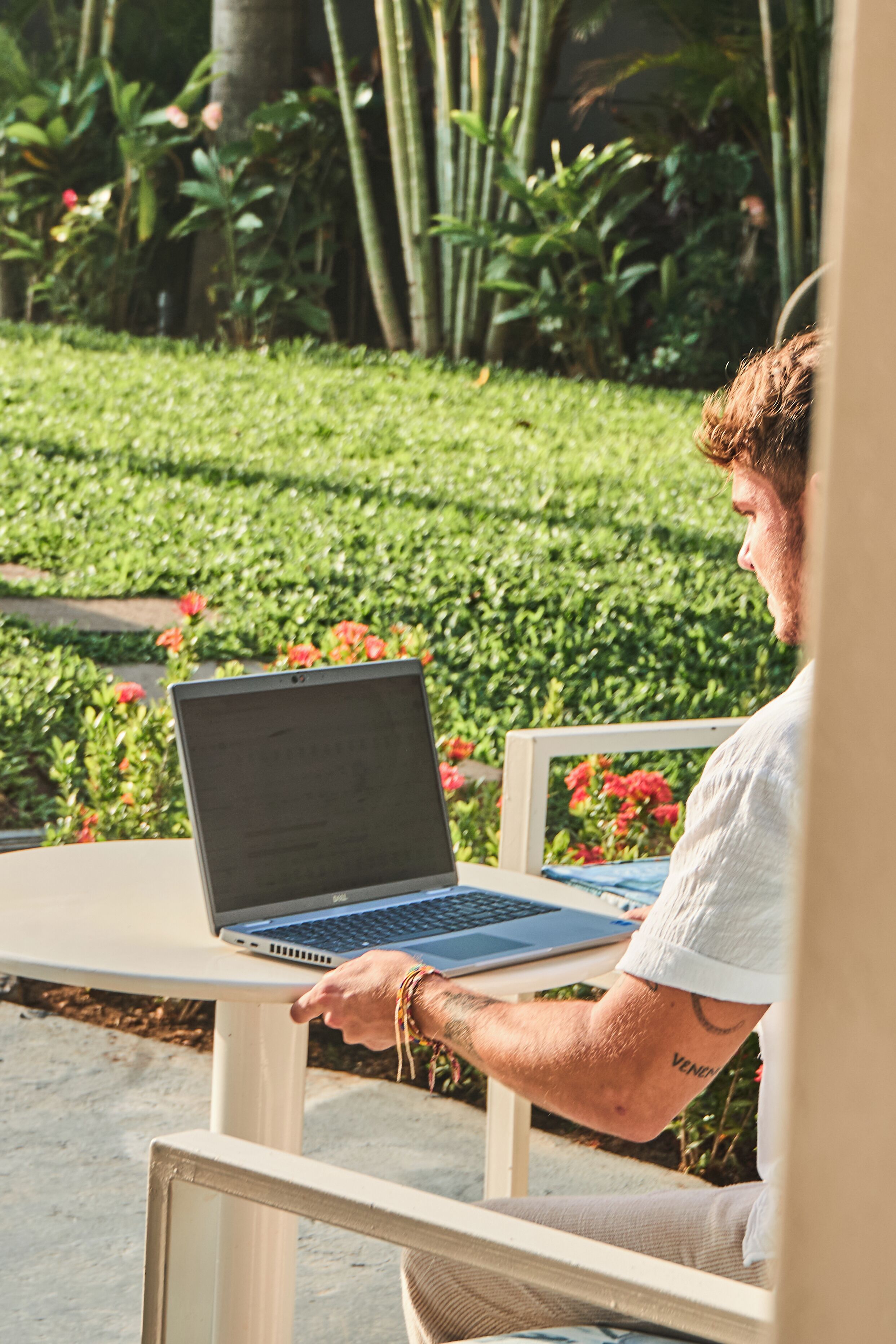 Une personne utilise un ordinateur portable sur une table à l’extérieur, avec de la verdure en arrière-plan.