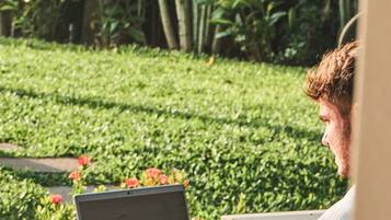 Une personne utilise un ordinateur portable sur une table à l’extérieur, avec de la verdure en arrière-plan.