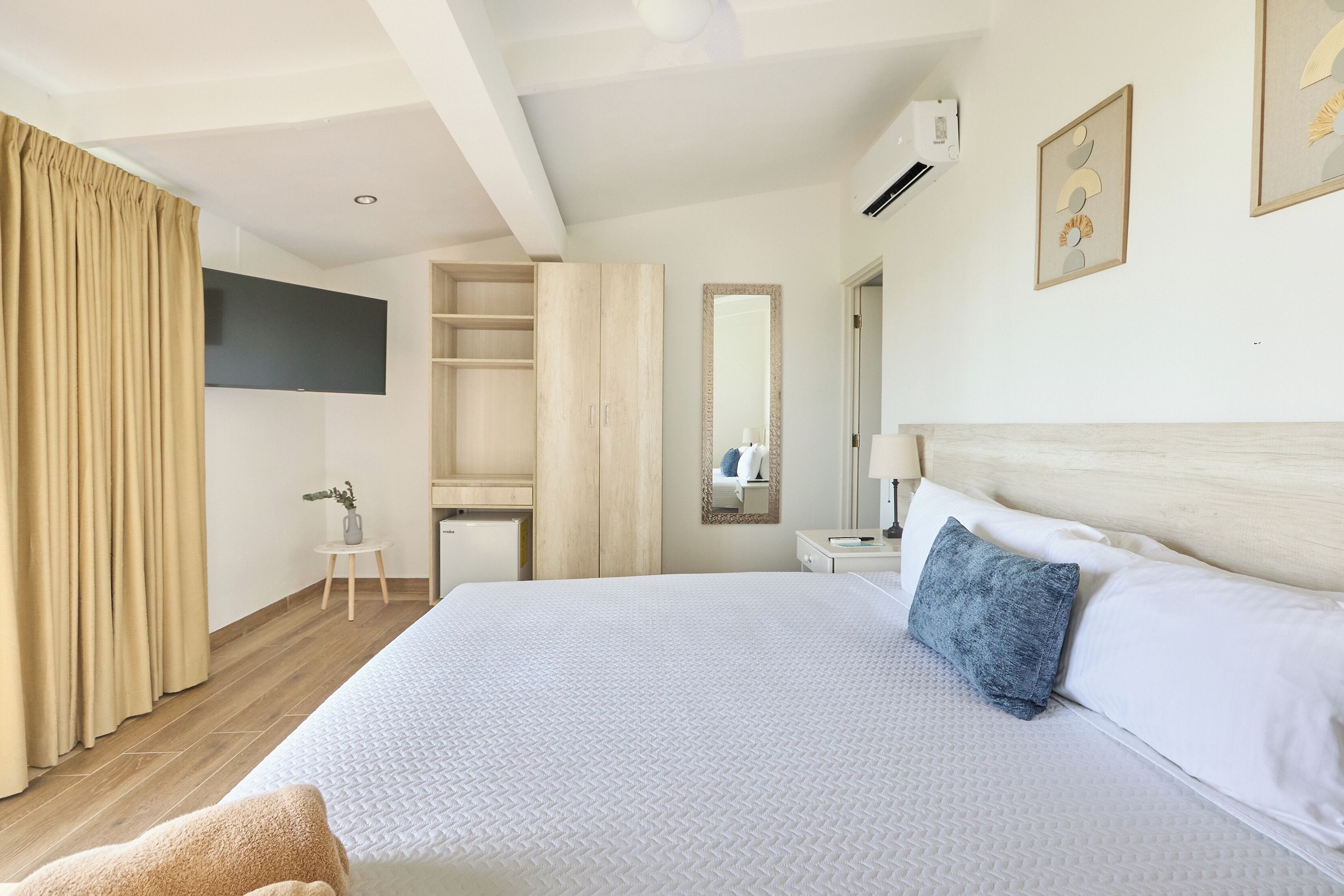 A hotel room with a large bed, a wardrobe, a desk, a mirror, and a TV mounted on the wall.