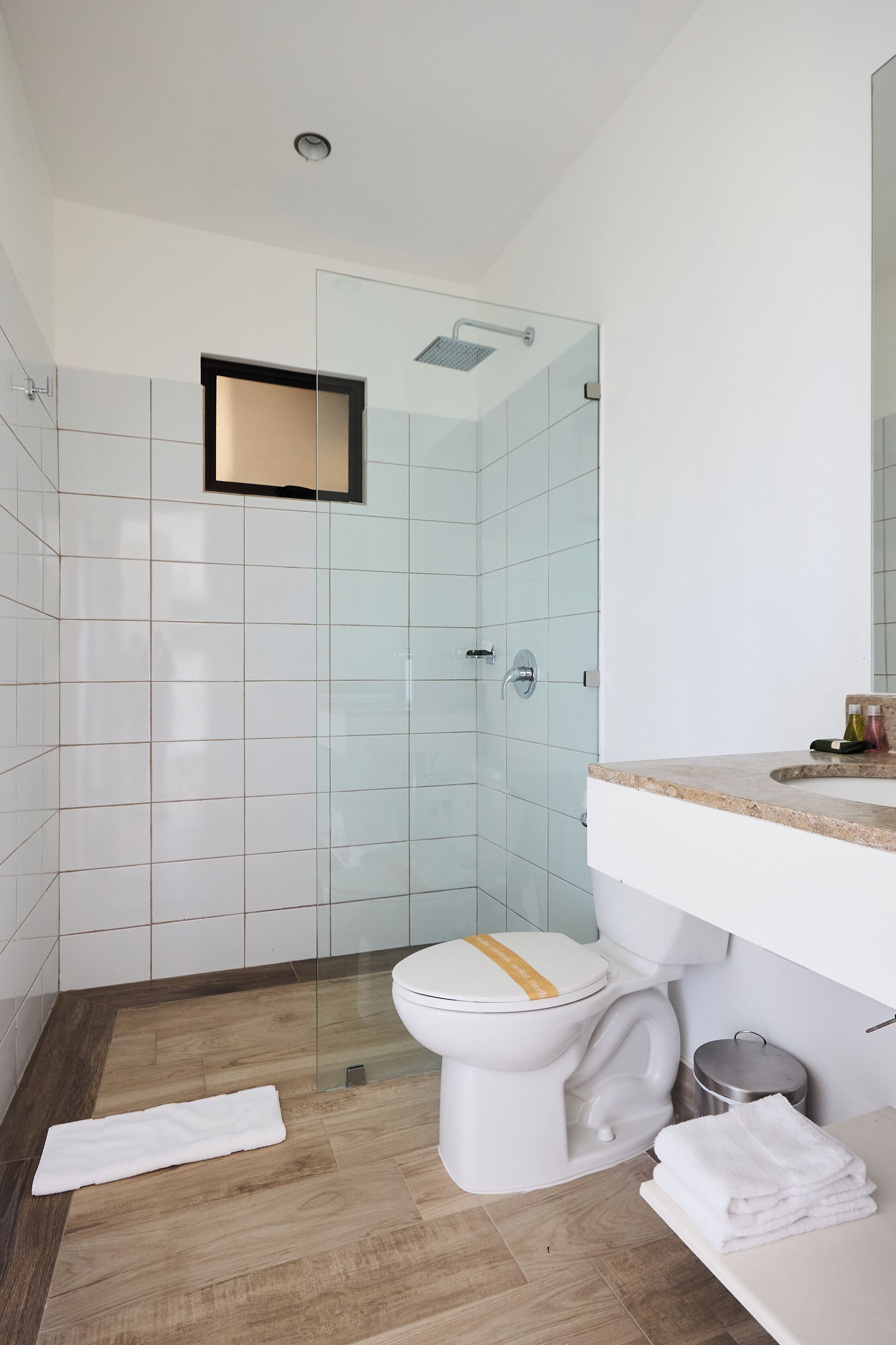Un baño moderno con cabina de ducha de vidrio, inodoro blanco y encimera color beige.