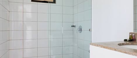 Un baño moderno con cabina de ducha de vidrio, inodoro blanco y encimera color beige.