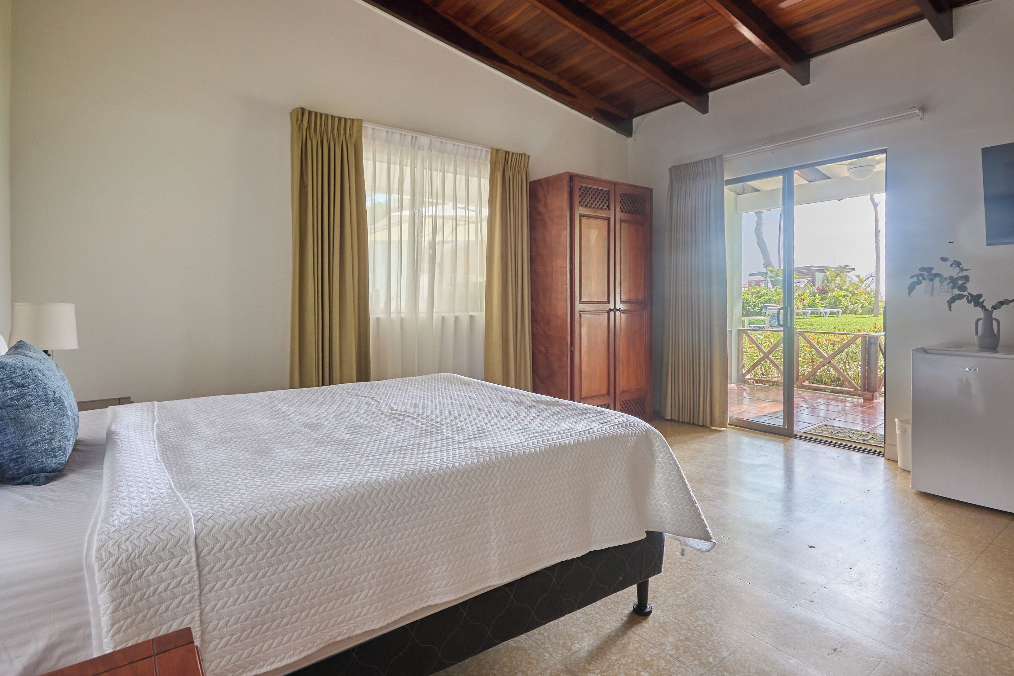 Un dormitorio con cama, armario de madera y vistas al exterior por un ventanal corredero.