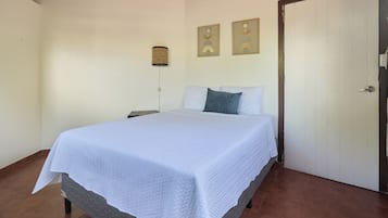 A bedroom with a bed, a nightstand, a wall-mounted lamp, and two framed pictures.