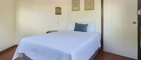 A bedroom with a bed, a nightstand, a wall-mounted lamp, and two framed pictures.