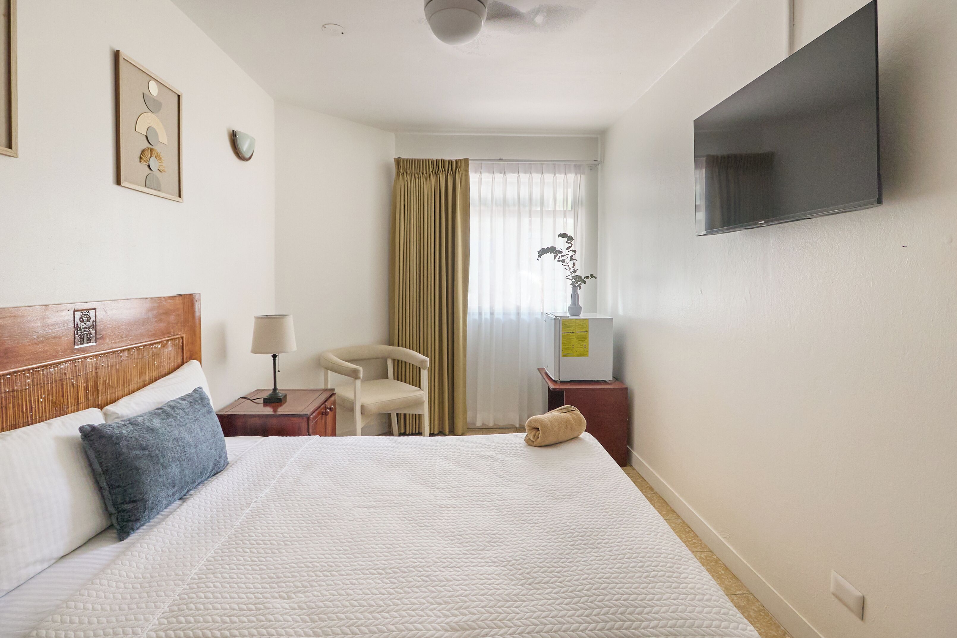 Ein Hotelzimmer mit Bett, Sessel, Schreibtisch, Fernseher und einem Fenster mit Vorhängen.