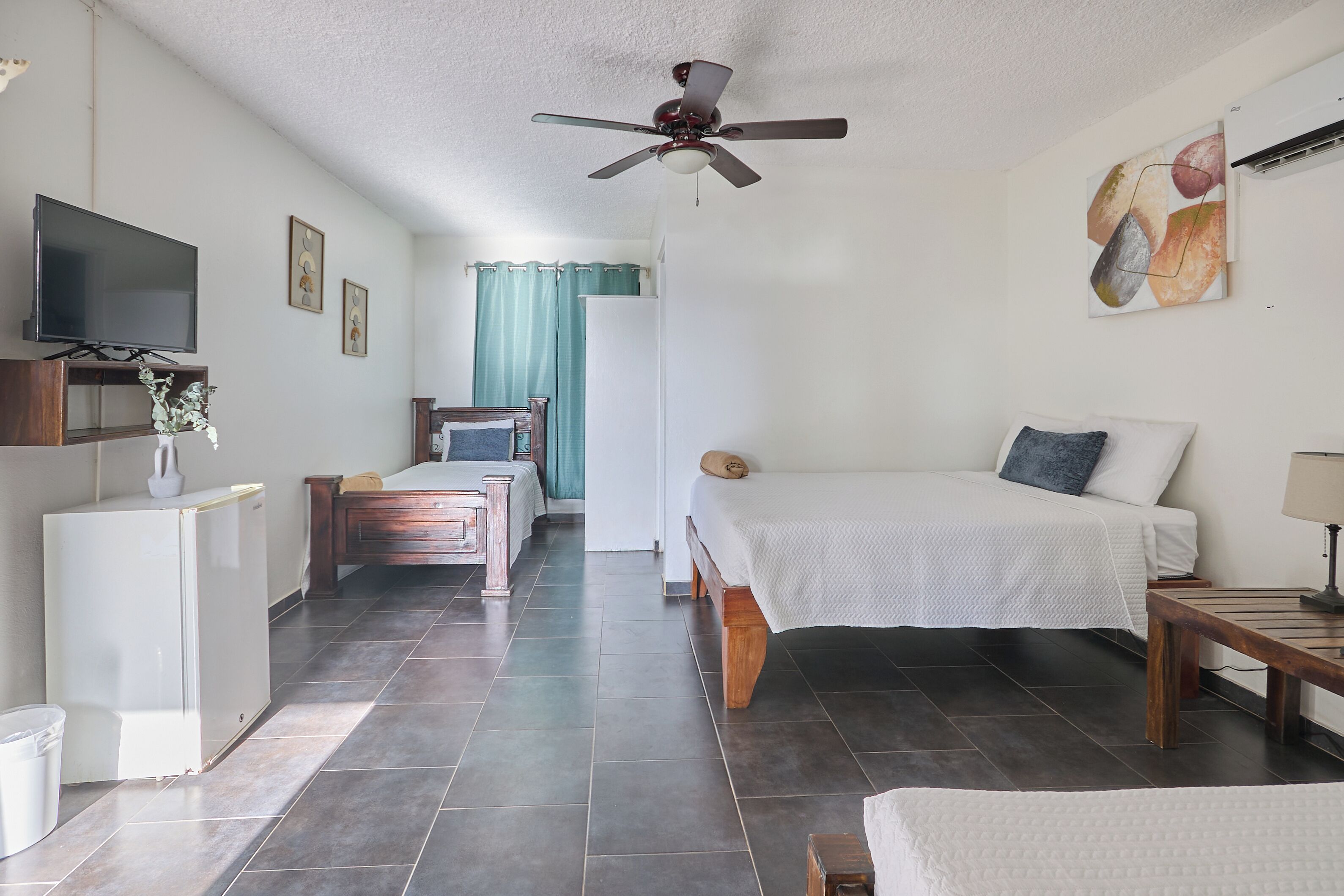 A hotel room with a bed, a desk, a TV, a ceiling fan, and a window with curtains.