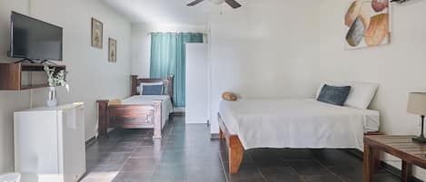 A hotel room with a bed, a desk, a TV, a ceiling fan, and a window with curtains.