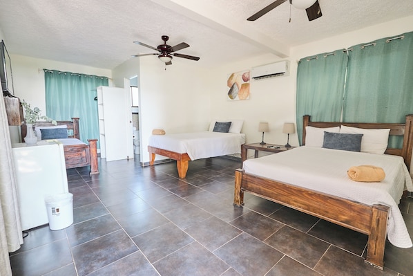 A bedroom with two beds, a ceiling fan, a white refrigerator, and a wooden nightstand. - Hotel Perla de la Playa (Tamarindo)