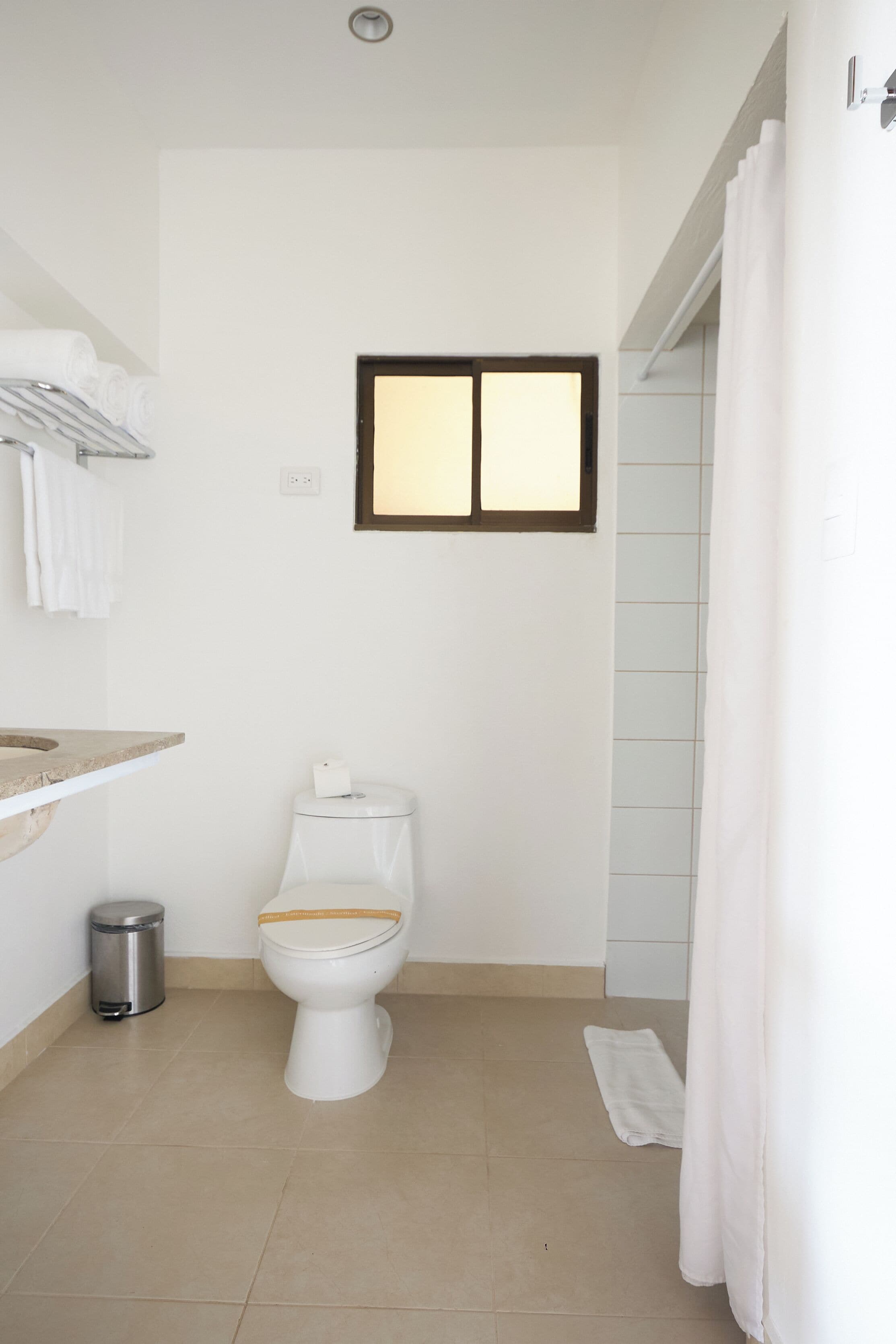 A bathroom with a toilet, a trash bin, a towel rack, and a shower curtain.