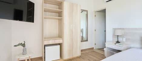 A modern bedroom with a bed, a wardrobe, a small table with a plant, a desk with a lamp, and a TV mounted on the wall.