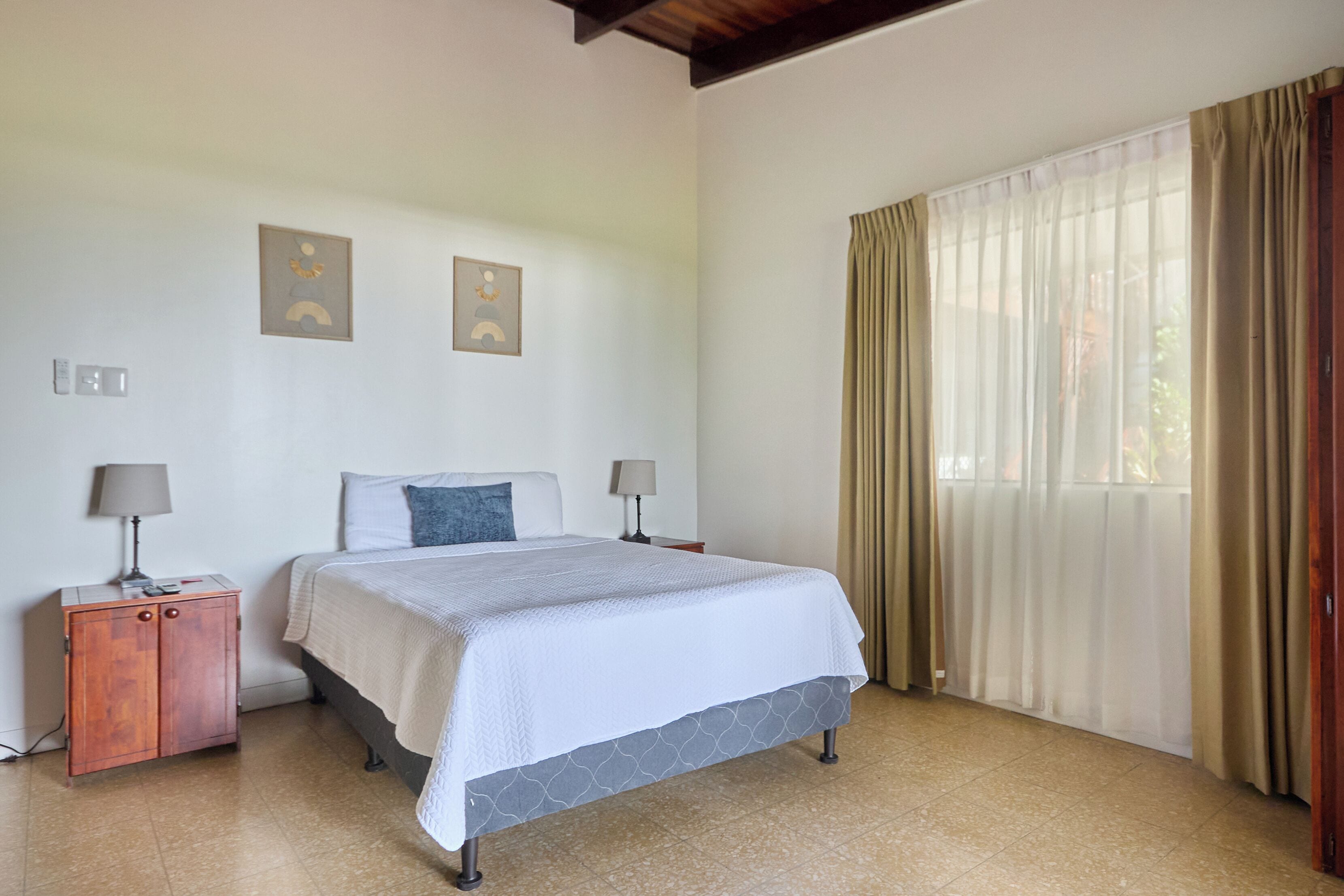 Una habitación de hotel con una cama, una mesita de noche, un armario y una ventana con cortinas.