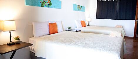 Habitación de hotel con dos camas, una mesita de noche con lámpara y obras de arte en las paredes.