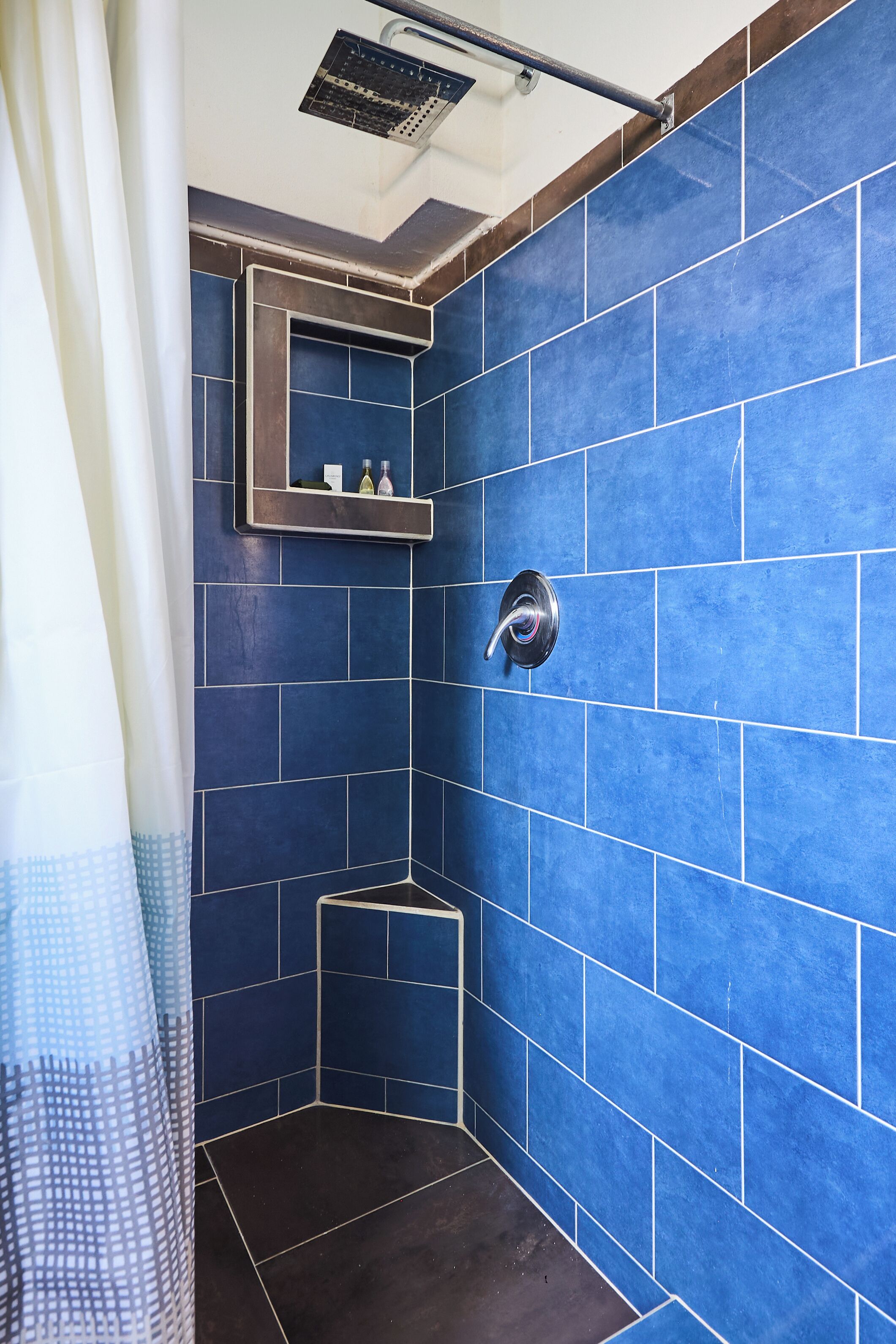 A bathroom with blue tiles, a showerhead, and a small shelf with toiletries.